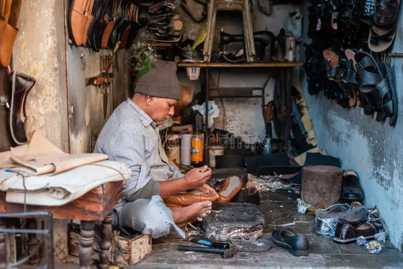 Cobbler hand-stitching footwear in a traditional street-side workshop